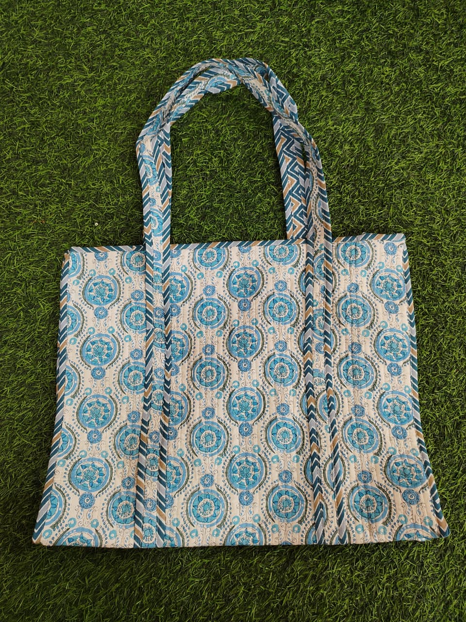 Tote bag with blue and beige pattern on a green grass background